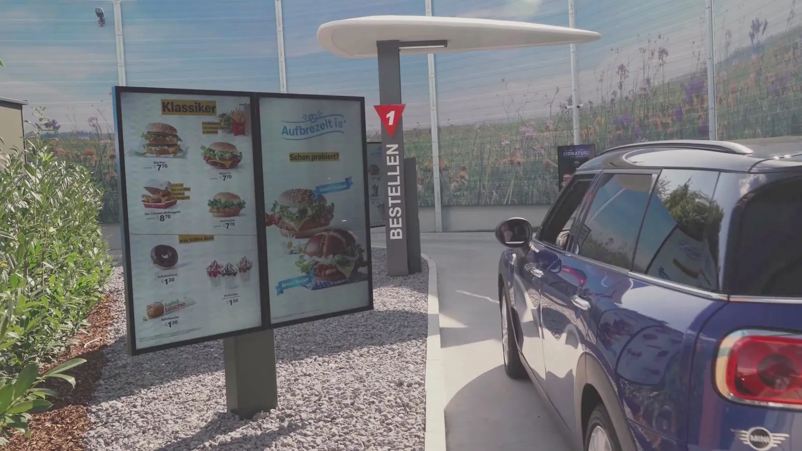A car at a drive-thru order point beside a digital menu board