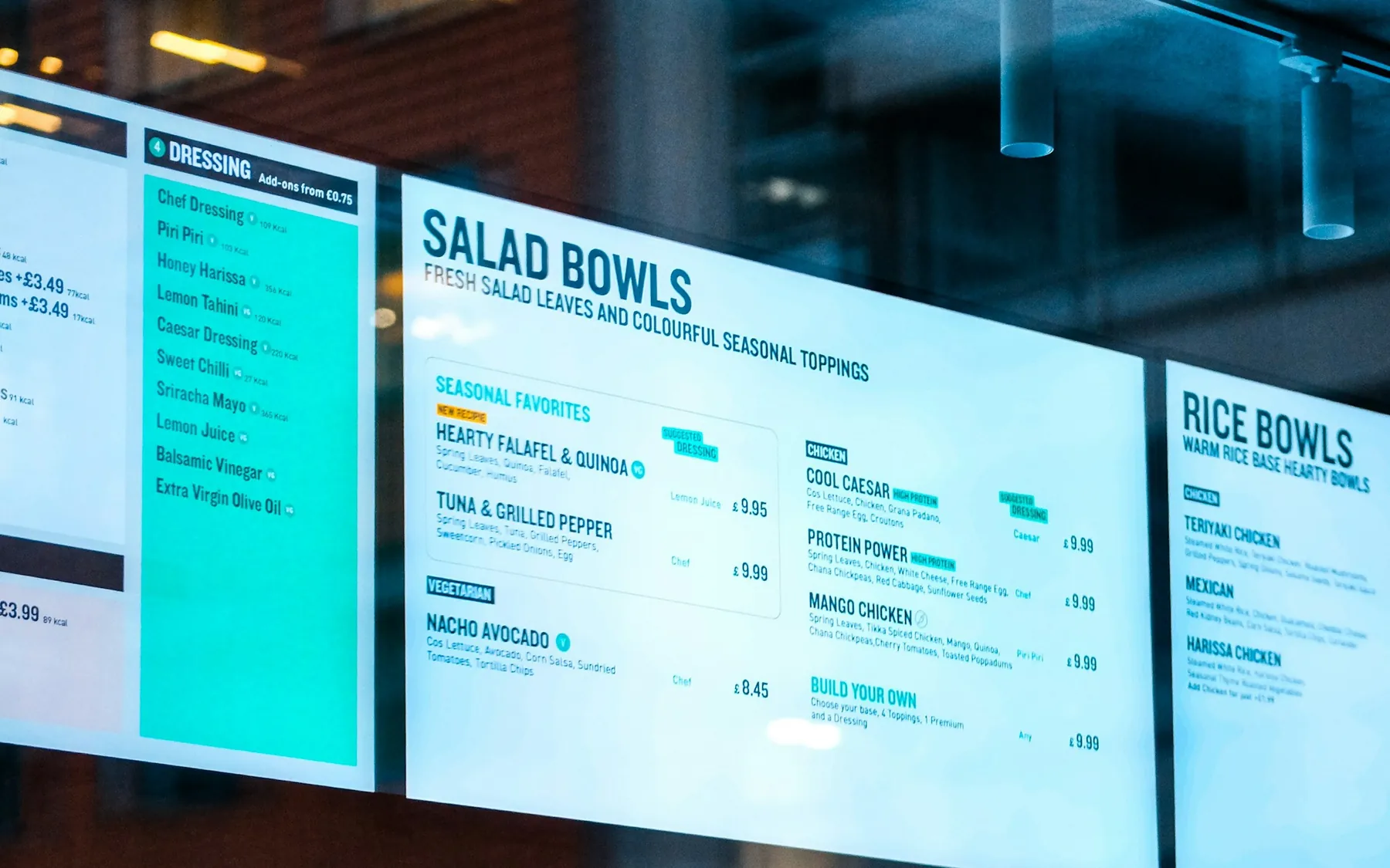 Digital menu boards showing salad and rice bowls in a restaurant window